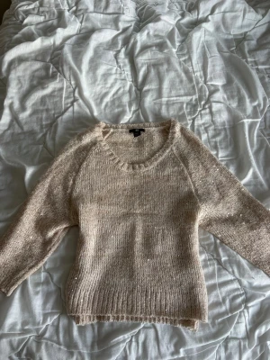 Beige stickad tröja från H&M - Mysig beige stickad tröja från H&M med rund halsringning och diskreta paljettdetaljer som ger lite extra glans. Tröjan har trekvartsärmar och ribbstickade muddar vid ärmslut och nederkant. Perfekt för lager på lager och chill dagar.