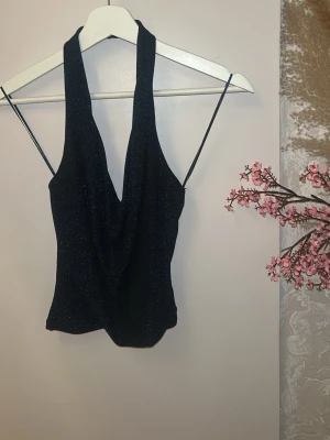 Glittrig svart halterneck topp - Snygg svart topp med glittrigt tyg och halterneck-modell. .