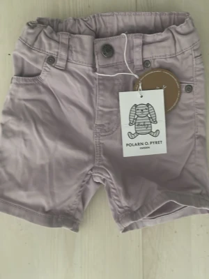 Ljuslila shorts från Polarn O. Pyret - Säljer ett par ljuslila shorts från Polarn O. Pyret i ekologisk bomull. Shortsen har klassisk femficksdesign, knapp och gylf framtill samt hällor för bälte. Perfekta för varma dagar och riktigt sköna att bära.