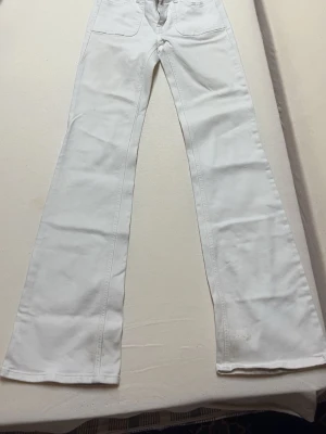 Vita utsvängda jeans med fickor - Säljer ett par vita jeans med utsvängda ben och stora fickor fram och bak. Jeansen har hög midja och klassisk femficksdesign. 