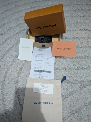 Lv svart monogram armband - Säljer ett svart armband från Lv med ikoniskt monogrammönster och silverfärgat LV-spänne. Armbandet är gjort i läder och levereras med originalpåse, box och äkthetskort. En riktigt snygg accessoar för dig som gillar designerstil.