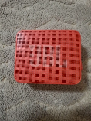 Röd JBL bärbar Bluetooth-högtalare - Snygg röd bärbar högtalare från JBL med tydlig logga på framsidan. Kompakt och rektangulär design med knappar för volym, Bluetooth och play/pause på ovansidan. Perfekt för att ta med sig överallt och spela musik trådlöst via Bluetooth.