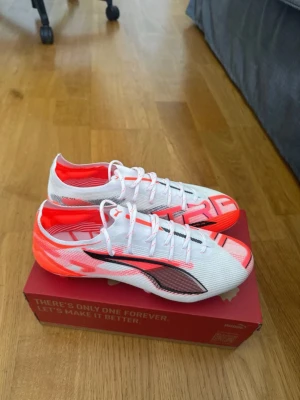 Vita och orangea Puma fotbollsskor - Snygga fotbollsskor från Puma i vitt med orangea och svarta detaljer. Modell Puma Ultra 5 Ultimate FG