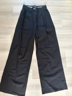  Alo byxor  - Snygga svarta byxor från Alo med bred resår i midjan och extra vida ben. Perfekta för en avslappnad och trendig stil. 