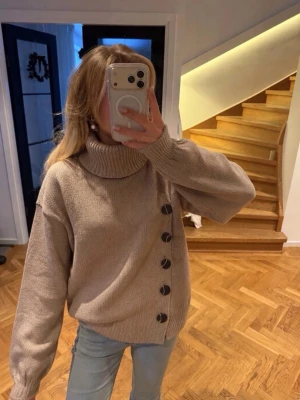 Beige stickad polotröja med knappar - Säljer en beige stickad polotröja med stora svarta knappar längs sidan. Tröjan har en hög krage, avslappnad passform och långa ärmar. Perfekt för lager på lager och riktigt mysig till kalla dagar. Storlek xs/s oversized💓💓