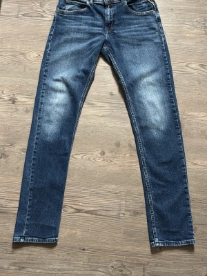 Blå jeans från Replay Wally's - Snygga blå jeans från Replay, modell Wally's, med klassisk femficksdesign och raka ben. Jeansen har slitningar och ljusare partier framtill för en trendig look. Tillverkade i denim med kontrastsömmar och metallknapp i midjan.