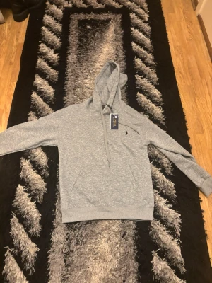 Grå hoodie från Polo Ralph Lauren Storlek S - Snygg grå hoodie från Polo Ralph Lauren med klassisk huva och dragsko. Tröjan har en liten broderad logga på bröstet och ribbade muddar vid ärmar och nederkant. Perfekt för en chill och avslappnad stil. Pris kan diskuteras 