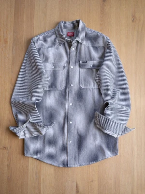 Randig overshirt från DePalma - Snygg långärmad overshirt från DePalma med svartvita ränder. Skjortan har två bröstfickor med knappar och klassisk krage. Tillverkad i slitstark bomull, perfekt för en cool och avslappnad stil. En knapp har lossnat, se bild. 