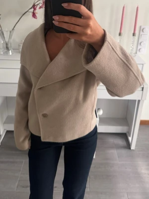 Beige kappa - Snygg beige kappa från Gina Tricot med bred, omlott krage och knäppning framtill. Nypris: 700kr