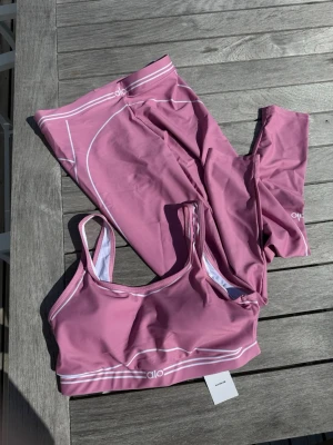 Alo Yoga Träningsset – Rosa (storlek M) - Alo Yoga-set med sport-bh och matching leggings i en fin rosa nyans. Storlek M. Helt nytt med lapparna kvar (NWT). Mjukt, stretchigt och skönt material med snygga vita randdetaljer – perfekt för träning eller lounge. Skickas snabbt 🚚💨 ✨ Skön passform och stilren design. 📩 Skicka gärna ett meddelande vid frågor eller prisförslag! 🛍️ Bundle-rabatt upp till 20%! 📦 Skickas samma eller nästa dag. 