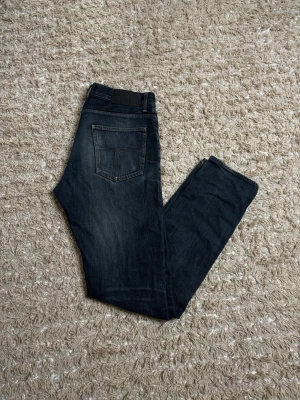 Mörkblå tiger of sweden jeans - Snygga mörkblå slim fit jeans med klassisk femficksdesign och diskreta slitningar. Jeansen har en bakficka med dekorativ söm och bälteshällor i midjan. Perfekta för en avslappnad och trendig look. Fits W32-33