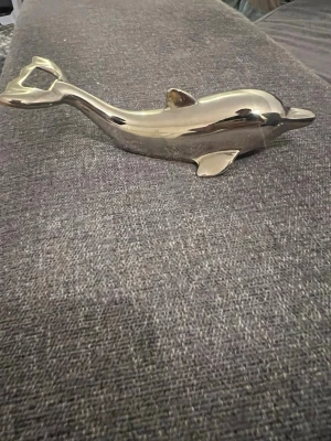 Delfinformad flasköppnare i metall - Säljer en stilren flasköppnare i form av en delfin. Den är tillverkad i blank metall med en silvrig finish och har en smidig öppnare baktill vid stjärtfenan. Perfekt som rolig detalj till köket eller festen.