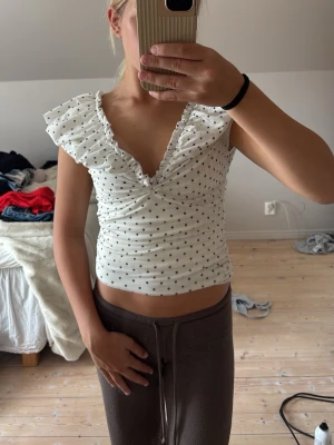 Vit prickig topp med volang - Söt vit topp med svarta prickar och volangdetaljer vid axlarna. Köpt för 400 och har använt den 1 gång.