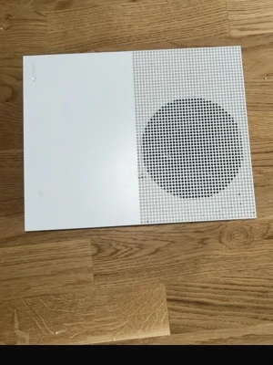 Xbox One S vit spelkonsol - Säljer en stilren vit Xbox One S spelkonsol med modern design och rund ventilationsyta på ovansidan. Konsolen har flera portar på baksidan för HDMI, USB och nätverk. Perfekt för gaming och streaming.