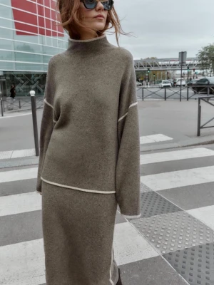 Brun stickad tröja med polokrage - Snygg brun stickad tröja med hög polokrage och vida ärmar. Tröjan har vita kontrastsömmar vid ärmar och nederkant som ger en modern touch. Perfekt för dig som gillar en avslappnad men trendig stil. Materialet ser mjukt och skönt ut.