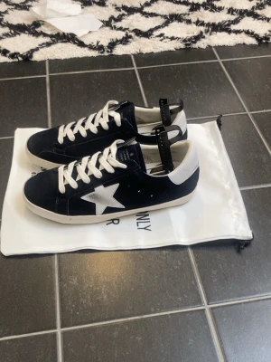Golden Goose Super-Star i marinblå mocka. - 43 – Nytt skick  Beskrivning:  Äkta Golden Goose Super-Star i marinblå mocka.  Använda 2 gånger och väl omhändertagna. Snygga premium-sneakers som passar perfekt till både vardag och streetwear.  Detaljer: ✅ 100% äkta Golden Goose ✅ Modell: Super-Star ✅ Storlek: EU 43 ✅ Färg: Marinblå ✅ Material: Mocka, läder och gummisula ✅ Originalkartong och dustbag ingår ❌ Kvitto saknas  Skorna är rena och redo att användas.  Säljes då de inte längre används.  📦 Snabb frakt 💬 Hör gärna av dig vid frågor ell