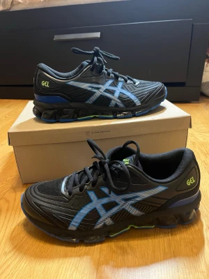 Svarta Asics sneakers med blå detaljer - Säljer dessa populära ASICS Gel-Quantum 180 som är svarta och blåa och har storlek 43.5. Dessa skor är designad för komfort och stöd. Skon har en svart ovandel med blåa detaljer och en sula med GEL-teknologi för stötdämpning. Yttersulan är mönstrad för att ge bra grepp. Skorna har lite skador runt gummit på sidan av skon som endast syns på nära håll, men det är inget som påverkar varken komfort eller utseende på långt håll. Vid frågor, extra bilder eller liknande är det bara att kontakta mig!