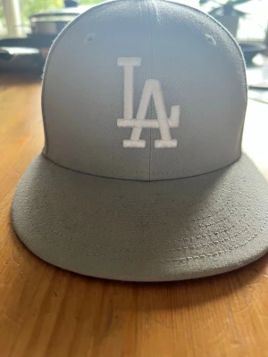 Grå LA 59FIFTY keps från New Era - Snygg grå keps från New Era med LA-logga broderad i vitt framtill. Modellen är 59FIFTY med rak skärm och klassisk passform🤩 Kepsen är tillverkad i ett slitstarkt tyg och har detaljer på insidan med 59FIFTY-band😅 