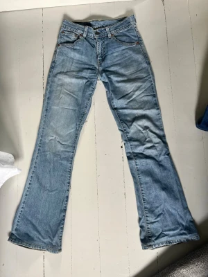 Ljusblå bootcut jeans Levi's - Säljer ett par ljusblå Levi's jeans med bootcut-ben. Jeansen har en vintagekänsla med slitningar och är tillverkade i denim. Passar perfekt för en avslappnad och trendig stil. Lite smutsiga längst ner. W 25