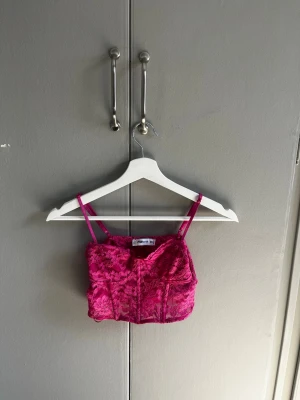 Rosa spetsig korsettopp - Snygg rosa korsettopp i storlek XS. Toppen har tunna axelband och är täckt av blommig spets som ger en romantisk vibe. Perfekt att styla med höga jeans eller kjol för en trendig look.