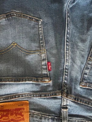 Levi's 501 ljusblå denimjeans - Klassiska Levi's 501 jeans i ljusblå denim med raka ben och femficksmodell. Jeansen har den ikoniska röda Levi's-lappen på bakfickan och patch i läder bak i midjan. Tillverkade i slitstarkt bomullsmaterial och passar perfekt till en avslappnad stil. 