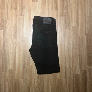 Jack & Jones jeans - Snygga svarta jeans med rak passform och klassisk femficksdesign. Jeansen har en enkel look utan slitningar och är tillverkade i ett mjukt denimtyg. Perfekta för dig som gillar en clean och stilren stil. De är aldrig använda