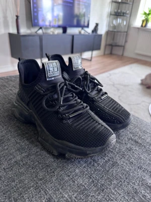 Svarta chunky sneakers Steve Madden - Säljer ett par svarta chunky sneakers från Steve Madden med stickad ovandel och tjock sula. Skorna har svarta skosnören, diskret logga på sidan och meshdetaljer för extra ventilation. Perfekta för dig som gillar streetstyle och vill ha bekväma skor med attityd.