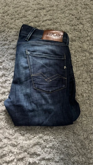 Mörkblå jeans från Replay - Snygga mörkblå jeans från Replay med klassisk femficksdesign och kontrastsömmar på bakfickan. Jeansen har en rak passform och är tillverkade i slitstarkt denimtyg. Perfekta för dig som gillar en tidlös och stilren look.