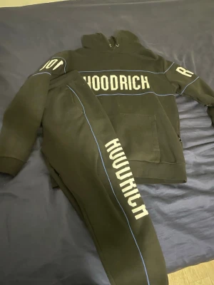 Hoodrich set  - Säljer ett svarta set  från Hoodrich med vit logga längs benet och tunna blå detaljer. Byxorna har en avslappnad passform och är gjorda i mjukt material, perfekta för chill dagar. Matchar med hoodie för en komplett streetwear-look. Användes bara ett par gången