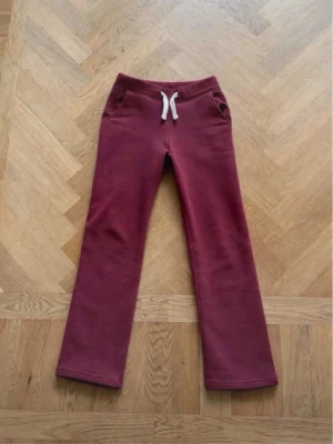 Vinröda mjukisbyxor med dragsko - Snygga vinröda mjukisbyxor med raka ben och vita dragsnören i midjan. Byxorna har två fickor fram och är gjorda i ett mjukt, bekvämt material som passar perfekt för chill dagar. Enkel och stilren design.