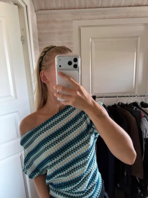 Randig offshoulder stickad topp - Säljer en soffshoulder topp med randigt mönster i blått, vitt och turkost. Toppen har en loose passform och är perfekt för dig som vill ha en unik och trendig look. Materialet känns mjukt och följsamt mot huden.