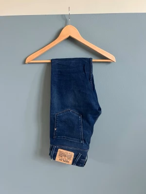 Mörkblå Replay anbass  - W28 och längd 32.          Snygga mörkblå slim fit jeans med fem fickor och klassisk knappgylf. Jeansen har lätt slitna detaljer och kontrastsömmar. Passformen är smal och benen är raka. Perfekta för en trendig och avslappnad look.