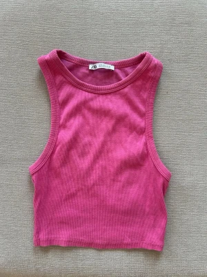Rosa ribbad croptop - Snygg croppad linnetopp i ribbad rosa bomull. Perfekt till jeans eller kjol för en chill och trendig look. Ärmlös design med rund halsringning och tight passform.
