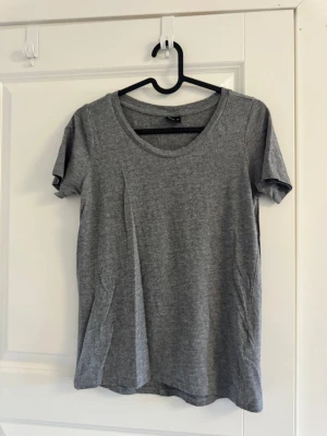 Grå basic t-shirt från Gina Tricot - En enkel och stilren basic grå t-shirt från Gina Tricot i mjukt material. T-shirten har rund halsringning och korta ärmar, perfekt till jeans eller shorts. Passformen är normal och tyget är tunt och skönt.