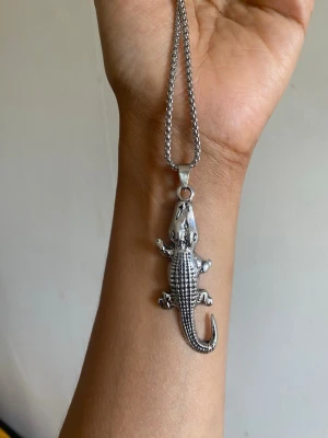 Silverfärgat halsband med krokodil - Unikt halsband med en detaljerad krokodilberlock i silverfärgad metall. Kedjan är medelgrov och berlocken har en cool, glänsande finish. Perfekt för dig som vill sticka ut med ett djurinspirerat smycke.