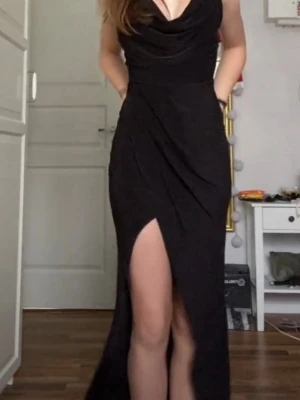 Svart långklänning med slits - Elegant svart långklänning med draperad urringning och hög slits framtill. Klänningen har smala axelband och en figurnära passform som framhäver siluetten. Perfekt för dig som vill ha en stilren och klassisk look. Perfekt att använda när du ska klä upp dig lite extra på någon fin tillställning. Klänningen är använd en gång och är i väldigt bra skick. 💗Ny priset på klänningen var ca 800kr. 