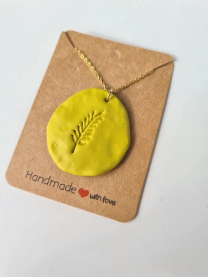 Handgjort halsband med berlock - Unikt halsband med en rund, olivgrön berlock i lera och ett ingraverat bladmotiv. Hänger i en tunn guldfärgad kedja, reglerbar upp till 45 cm. Gjort för hand av mig i polymerlera 