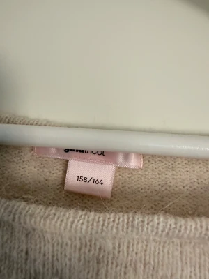 Ljusbeige stickad tröja Gina Tricot - Mysig ljusbeige stickad tröja från Gina Tricot i storlek 158/164. Tröjan har en enkel, rak passform med långa ärmar och rund halsringning. Perfekt för att hålla värmen under kyliga dagar och passar till det mesta i garderoben.
