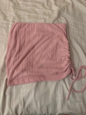 Rosa kortkjol  - Supersöt rosa kortkjol från Gina Tricot i mjukt frottématerial. Kjolen har snörning på sidan som ger en snygg rynkad effekt och gör att du kan justera passformen.
