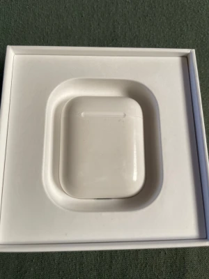 Vita trådlösa hörlurar med laddningsetui - Säljer ett par vita trådlösa hörlurar med tillhörande laddningsetui. Etuiet är kompakt och har en rundad form, tillverkat i plast. Perfekt för dig som vill ha smidiga hörlurar till mobilen eller datorn.