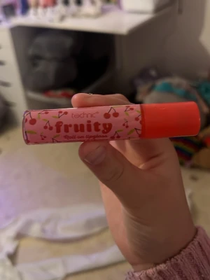 Technic Fruity Roll-on Läppglans - Säljer ett Technic Fruity roll-on läppglans med körsbärsmotiv på rosa bakgrund och orange lock. Läppglanset har en söt och lekfull design och är perfekt för dig som gillar fruktiga dofter och glossig finish.