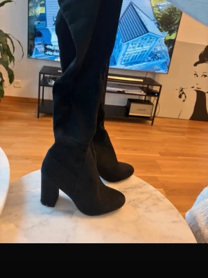 Svarta overknee stövlar med klack - Säljer ett par svarta overknee stövlar med hög, bred klack. Stövlarna är i mockaimitation och har en stilren, tight passform längs benet. Perfekta för att lyfta vilken outfit som helst och ger en trendig look. Märke: Tiamo  NYPRIS: 1200kr 
