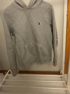 Grå hoodie  - Säljer en stilren grå hoodie från Ralph Lauren med broderad marinblå logga på bröstet. Hoodien har huva, magficka och ribbade muddar vid ärmar och nederkant. Perfekt för en avslappnad och snygg look. Storlek xs men sitter som xs-S. Skriv vid minsta fundering. Använd max 3 gånger