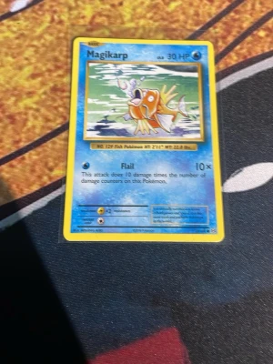 Magikarp Pokémonkort - Magikarp Pokémonkort med blå och gul ram. Kortet visar Magikarp i vatten och har 30 HP. Text och detaljer på engelska. Perfekt för samlare eller Pokémonfans.