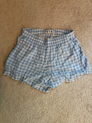 Rutiga blåvita pyjamasshorts - Säljer ett par pyjamasshorts i ljusblått och vitt rutmönster. Shortsen har resår i midjan och knytband för extra komfort. Perfekta för mysiga hemmakvällar eller lata morgnar. Skriv pm vid funderingar!☺️