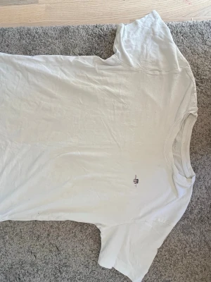 Vit t-shirt från Gant med logga - Klassisk vit t-shirt från Gant med liten broderad logga på bröstet. T-shirten har rund hals och korta ärmar. Tillverkad i mjuk bomull som känns skön mot huden. Perfekt basplagg till garderoben.