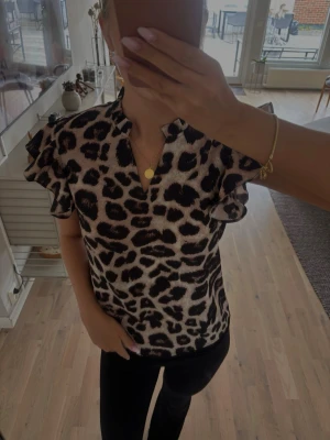 Leopardmönstrad blus med volangärm - Snygg blus med leopardmönster i beige och svart. Blusen har volangiga korta ärmar och en liten v-ringning vid halsen.  Aldrig kommit till användning tyvärr 