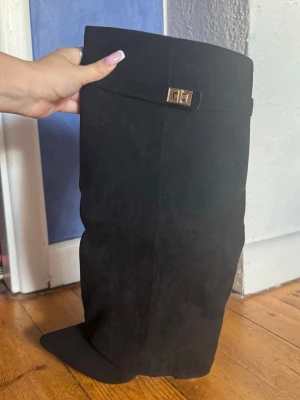Svarta boots från lululia - Säljer ett par svarta boots i mockaimitation med dekorativt guldfärgat spänne upptill. Stövlarna har en mjuk och slät yta samt en bredare passform upptill. Perfekta för dig som vill ha en stilren och trendig look. Använda en gång på en utekväll men absolut inget fel på dom.
