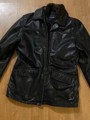 Läder/skinnjacka Park Lane - Park Lane skinnjacka i 100 % äkta läder, storlek L. Mycket välvårdad. Klassisk svart modell med mjuk fodrad krage, quiltat innerfoder och flera praktiska fickor. Rejäl och varm kvalitetsjacka.