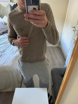 Beige stickad tröja Lyle & Scott - Snygg beige stickad tröja från Lyle & Scott med rund halsringning och den klassiska gula loggan på bröstet. Tröjan har en enkel och stilren design, perfekt för lager på lager. Materialet känns mjukt och bekvämt mot huden.